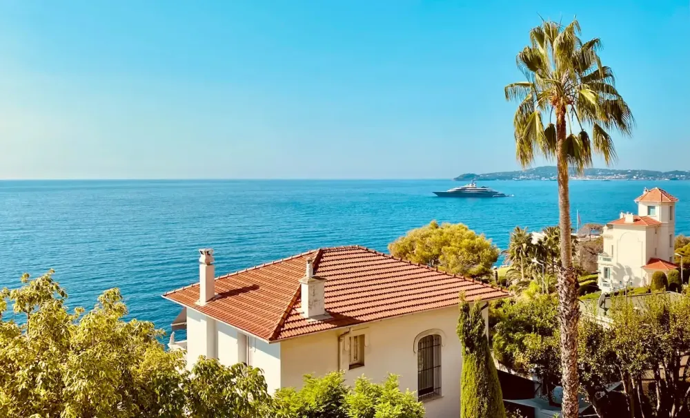 Mediterrane weiße Villa mit Terrakottadach am blauen Meer, umgeben von Bäumen.