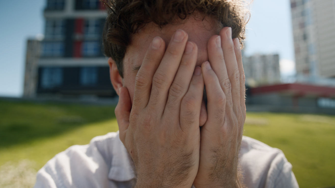 Close up tired unhappy Caucasian man covering face hands grief problems exhausted employee work male upset sad suffering pain stress guy businessman emotions business overworked city outside depressed