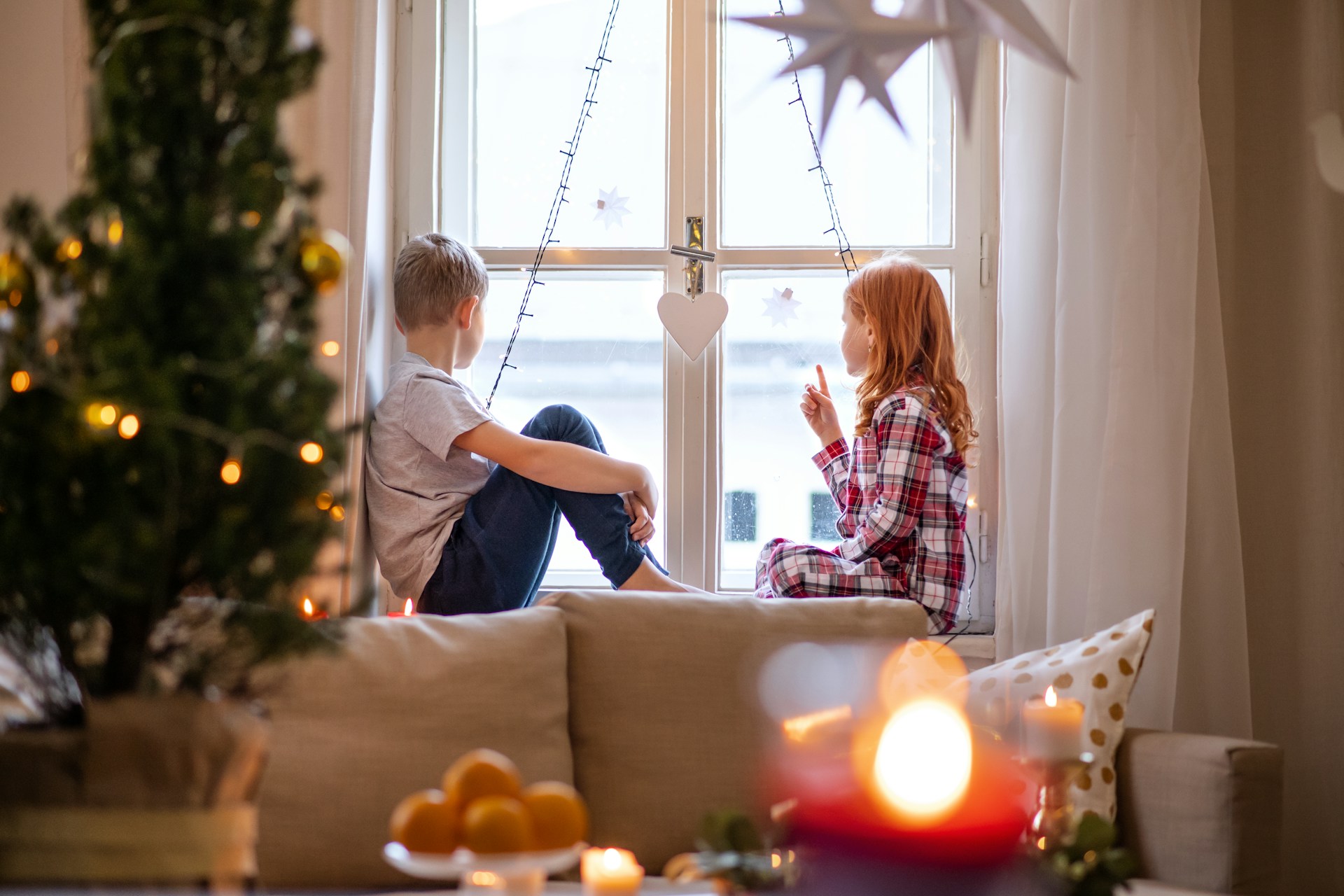 getty images via unsplash Zwei Kinder sitzen auf der Fensterbank neben Weihnachtsbaum