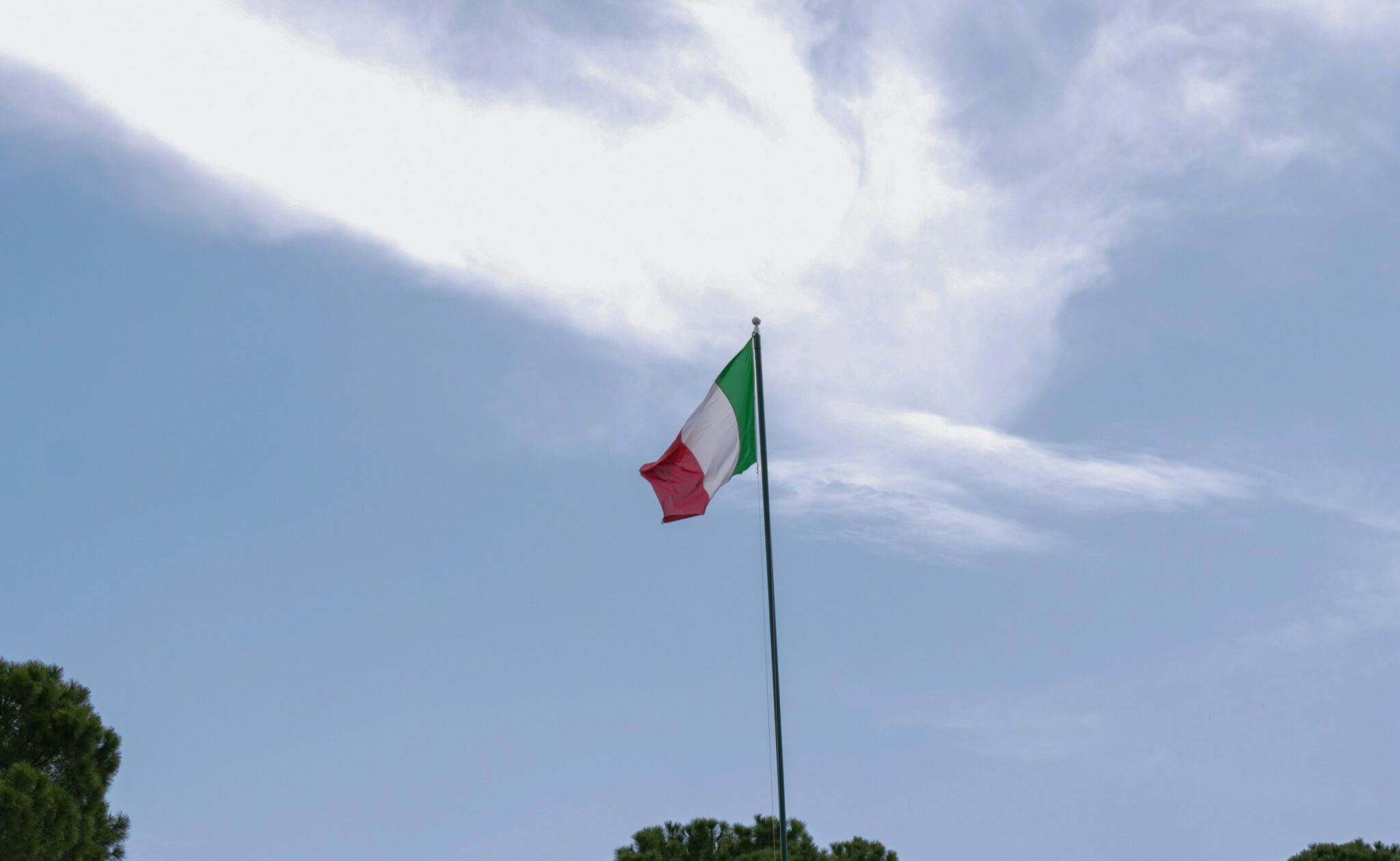 Szymonek_Wierzcholekutm_Unsplash Italien Flagge weht im Wind auf einer Bergspitze vor blauem Himmel