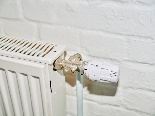 Close-up of a white radiator with a thermostatic valve against a brick wall, illustrating heating control tips for holiday rental landlords.
