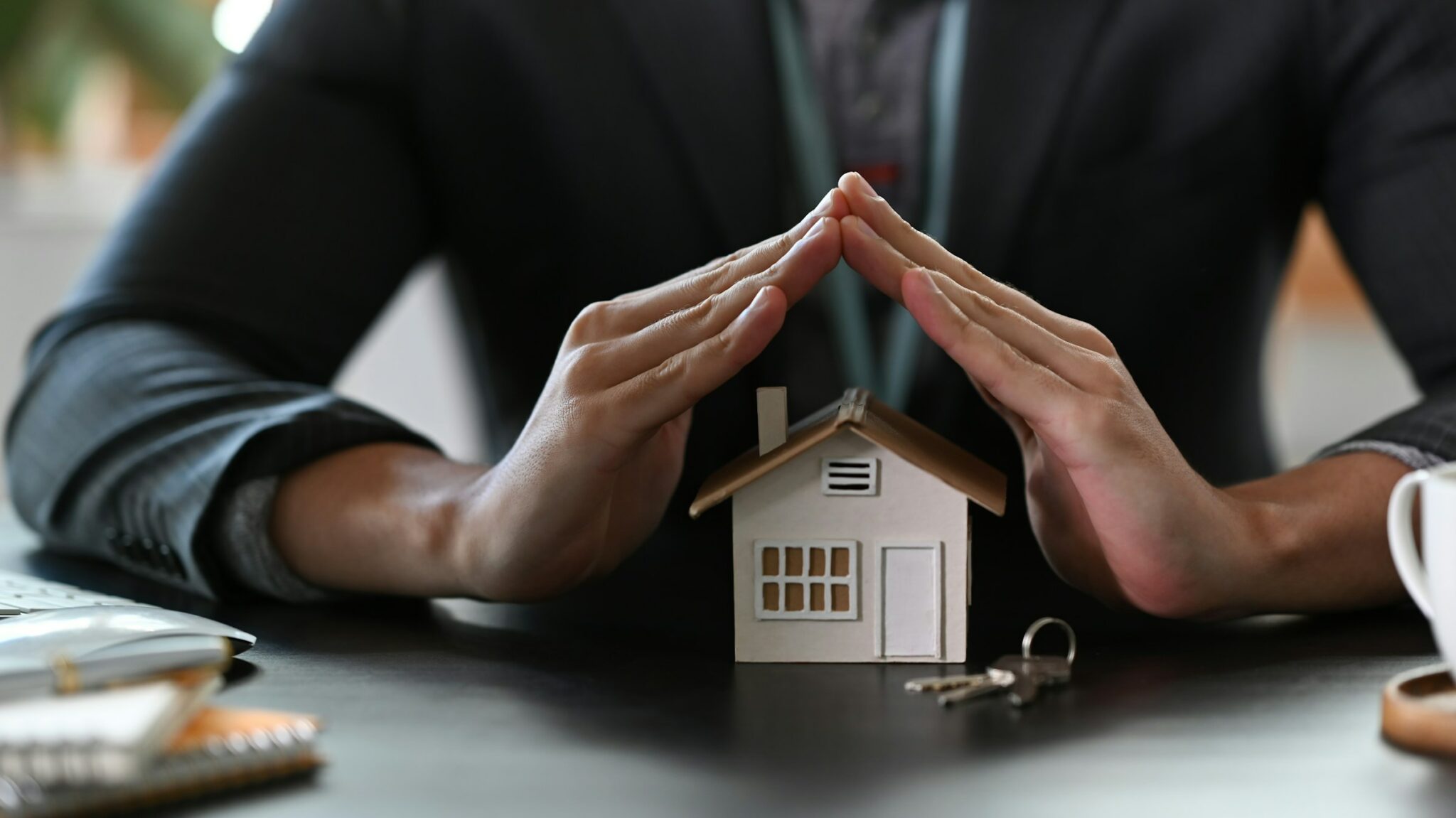 Mann hält schützend Hände über ein kleines Haus