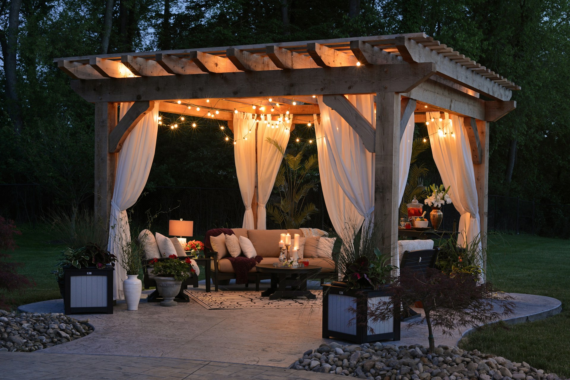 Holiday rental garden pergola with string lights, draped curtains and cosy outdoor seating at dusk