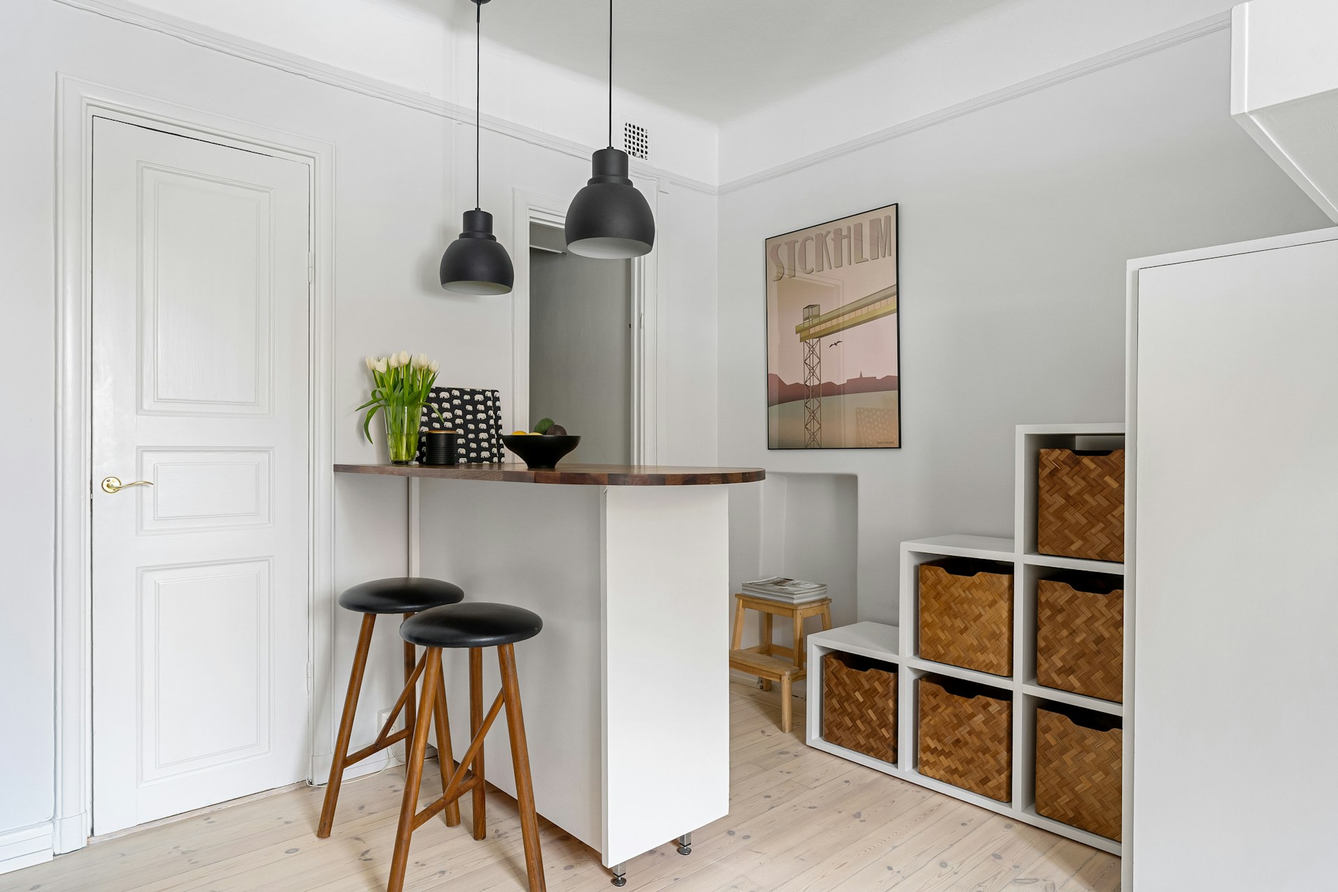 Compact holiday rental kitchen with breakfast bar, bar stools and modular storage unit with wicker baskets