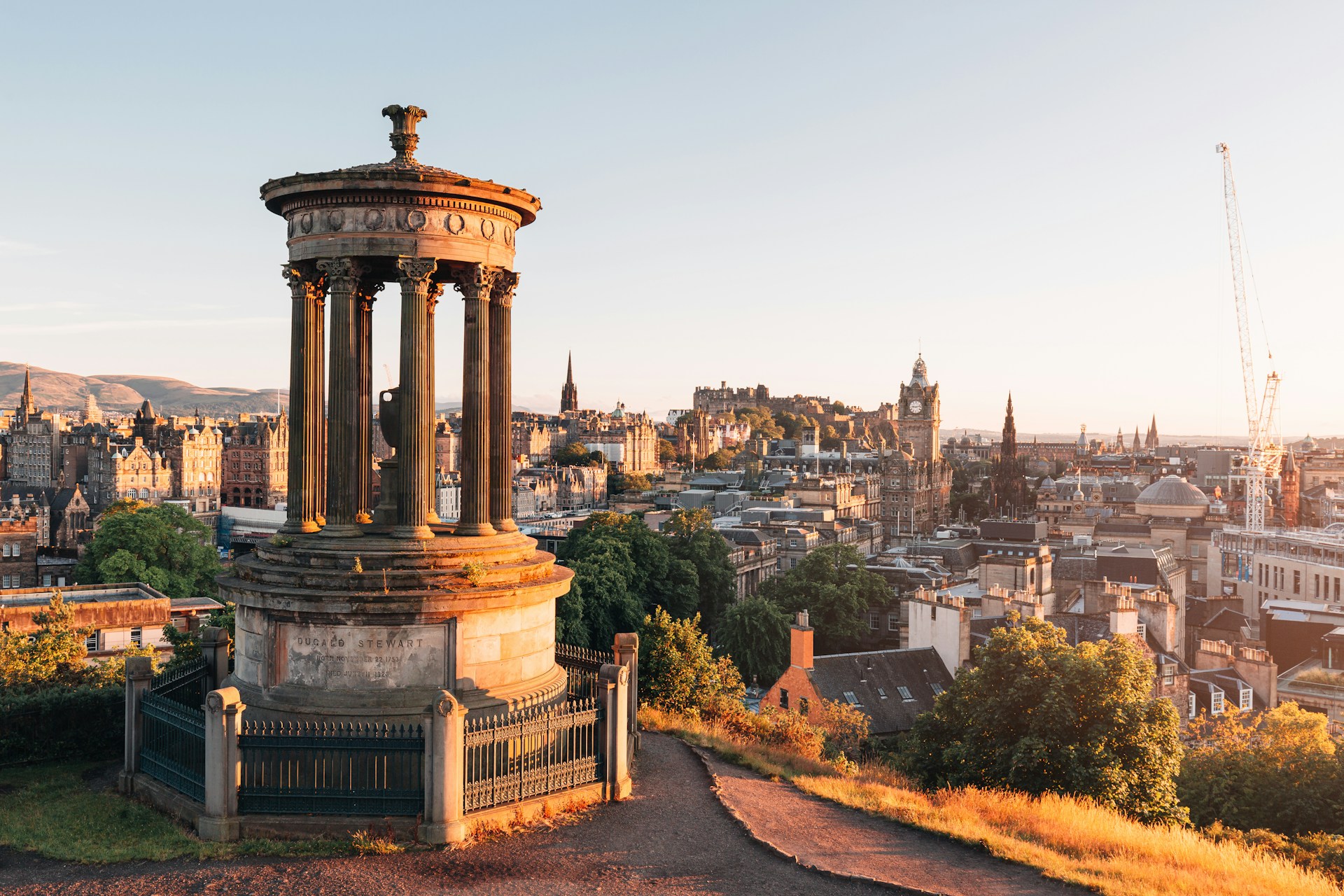 connor-mollison-d7_TtRp1s9s-unsplash View of Edinburgh's skyline at golden hour from Calton Hill, with the Dugald Stewart Monument in the foreground and Edinburgh Castle visible in the distance.