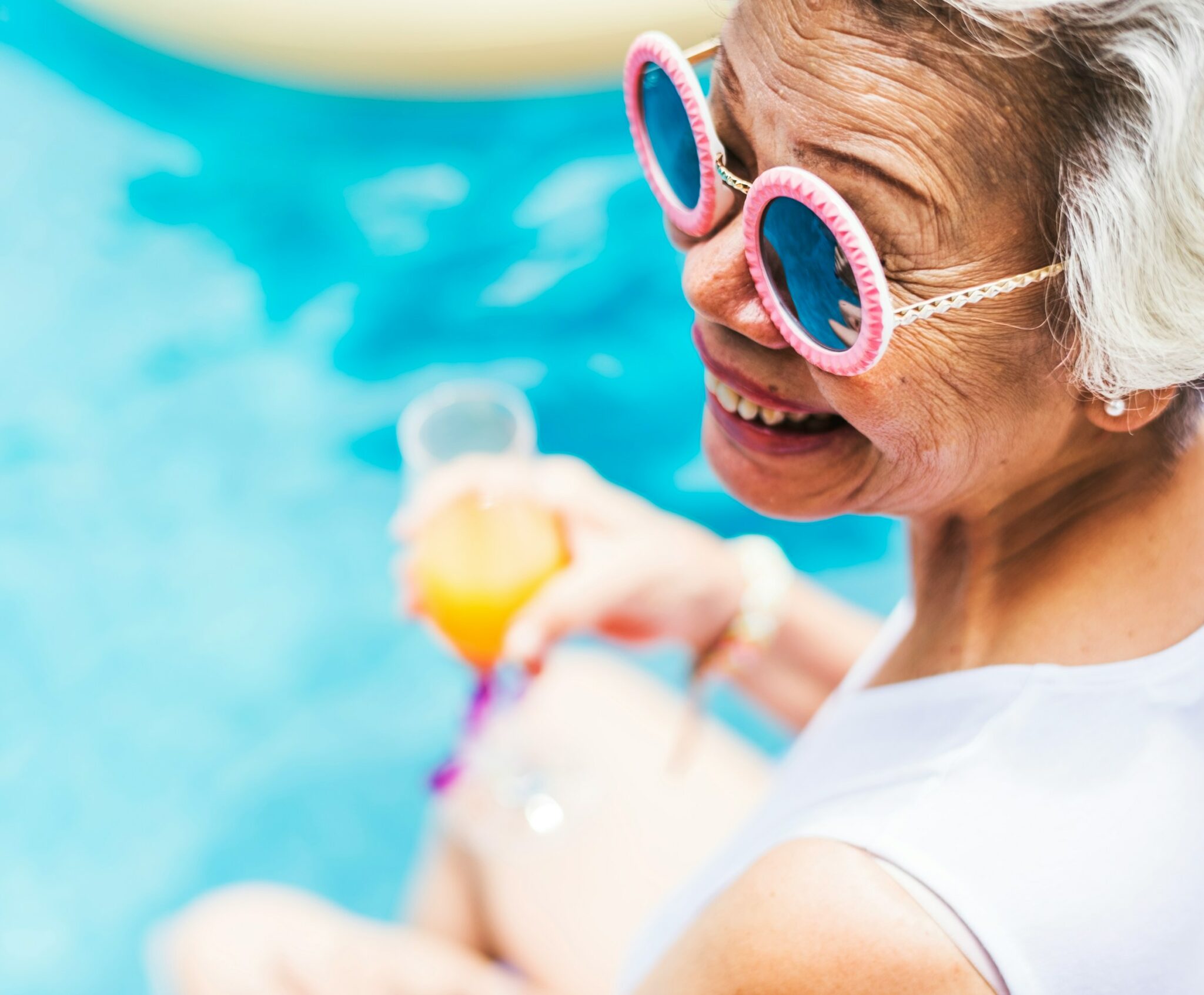 Curated Lifestyle via Unsplash Frau sitzt mit Sonnenbrille und Orangensaft am Pool