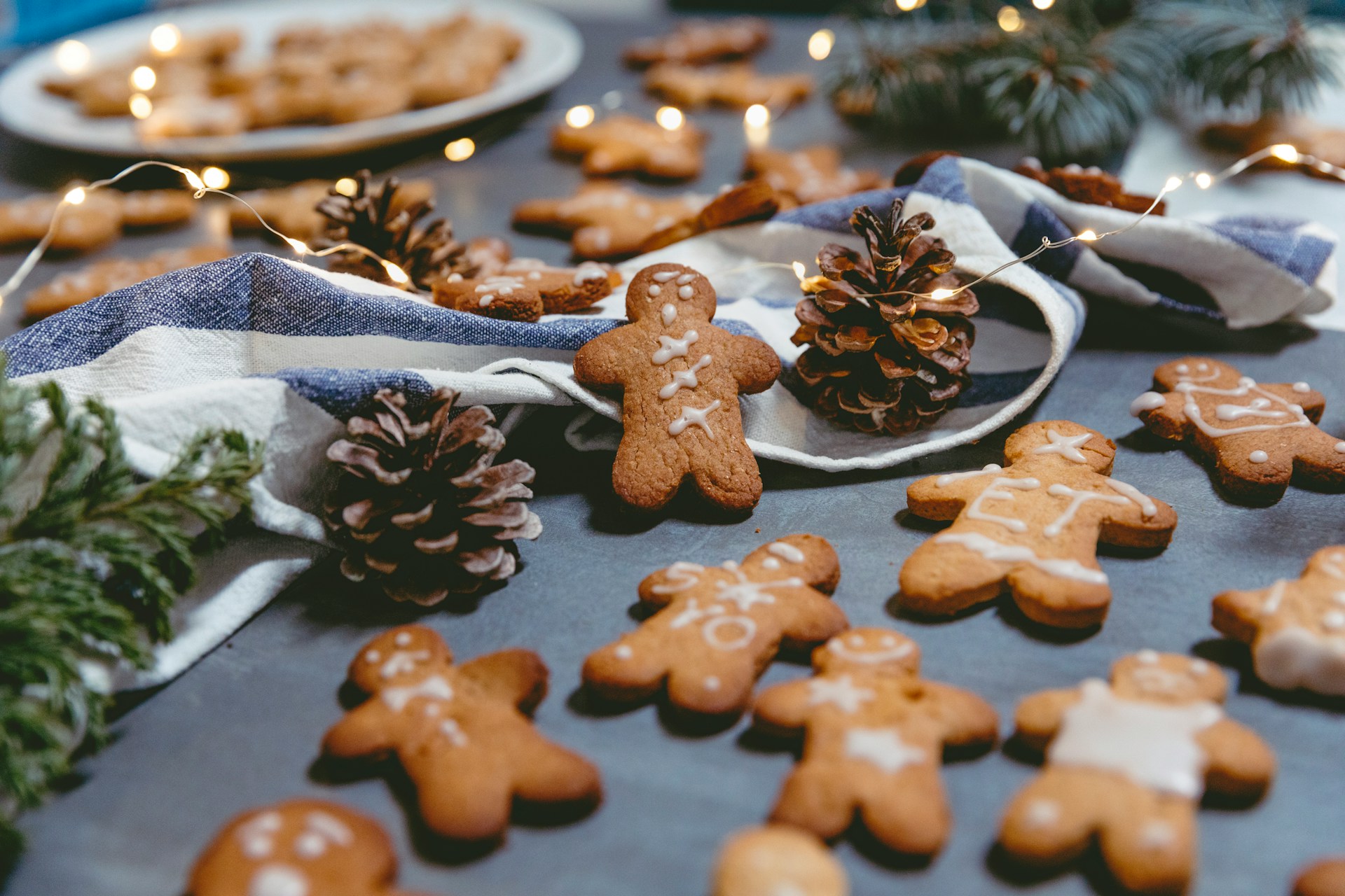 michele-purin-19F94SkMgU4-unsplash Freshly baked gingerbread men cookies scattered on a table with fairy lights and pinecones
