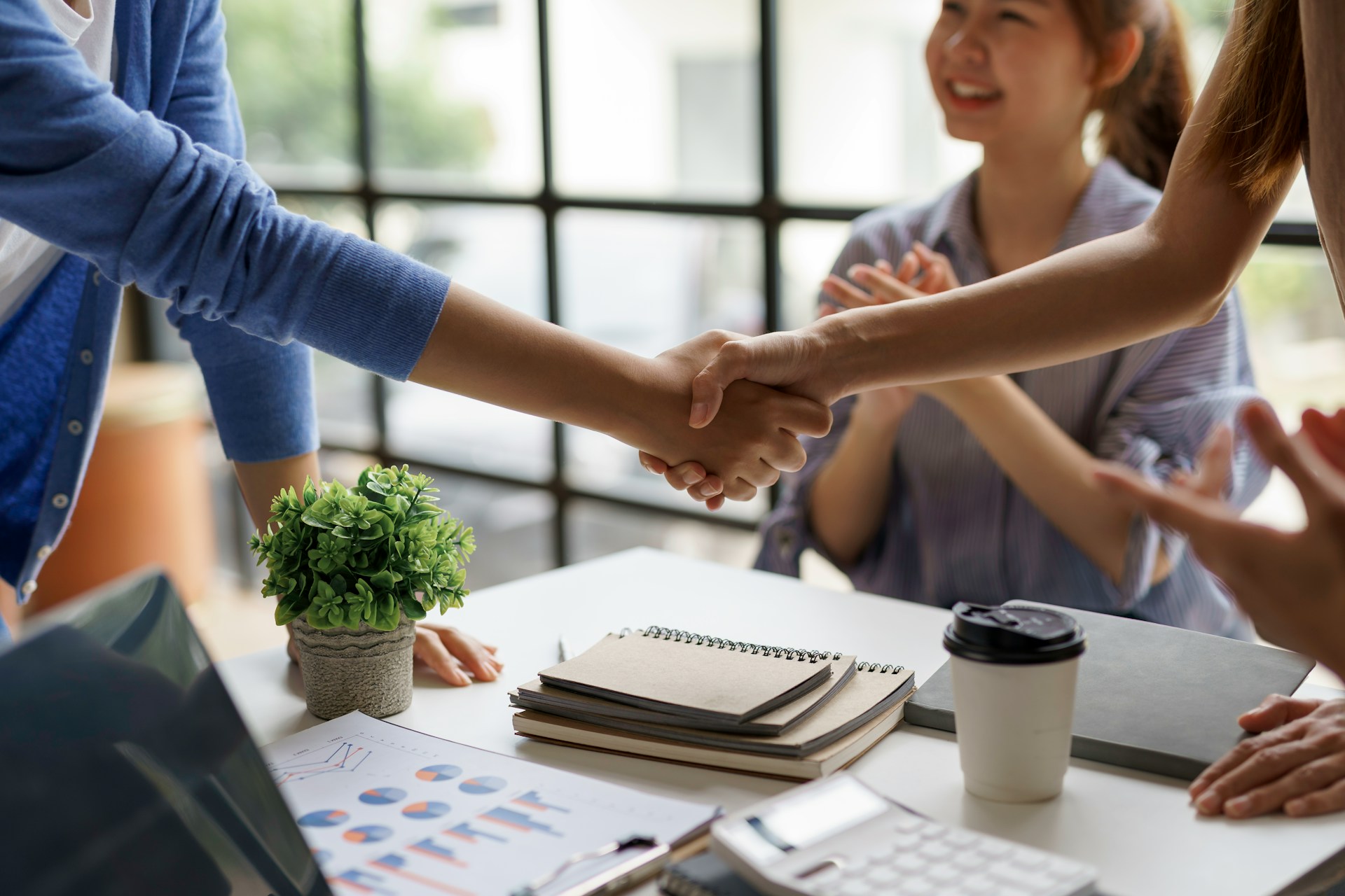 getty-images-NsRoGWKfSeE-unsplash Warm handshake between host and guest over a desk with notebooks and coffee