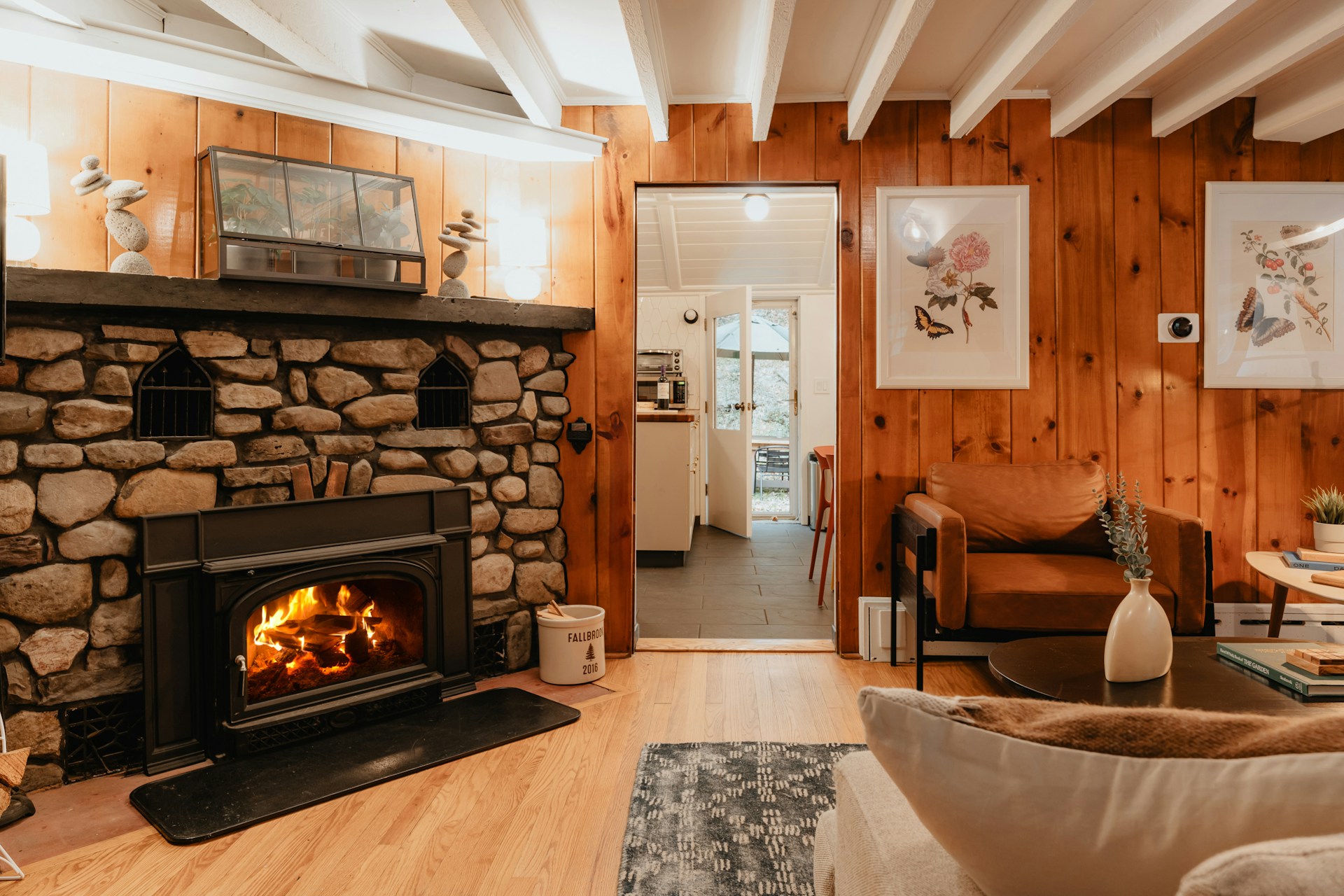clay-banks-ybLSV7sF7j8-unsplash Cozy cabin living room with a roaring stone fireplace insert, wood panelling, and comfortable armchairs