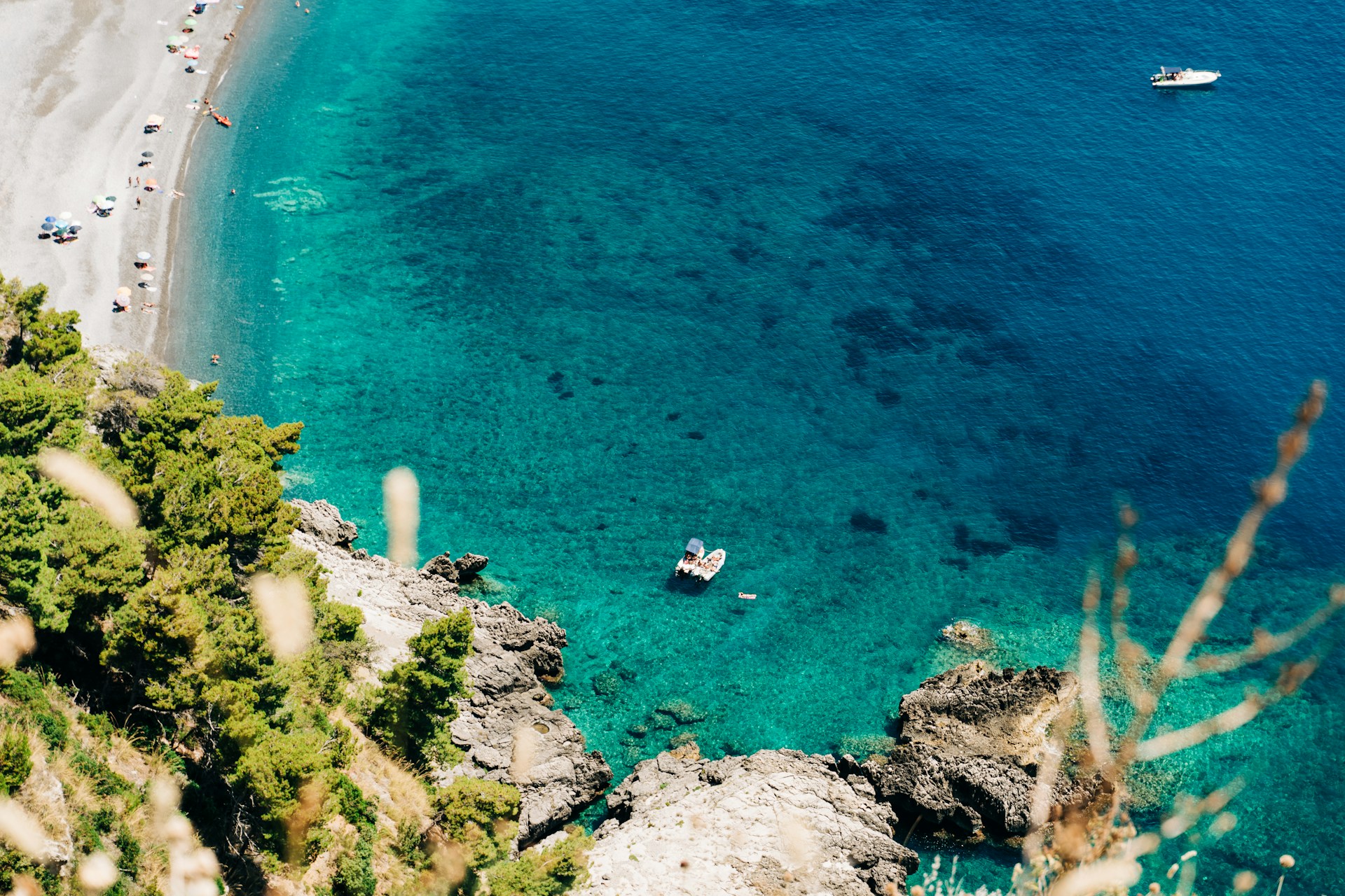 gabriella-clare-marino-Basilicata, Italy@unsplash Aerial view of a turquoise Mediterranean cove, with pine-covered limestone rocks and a pebble beach beyond