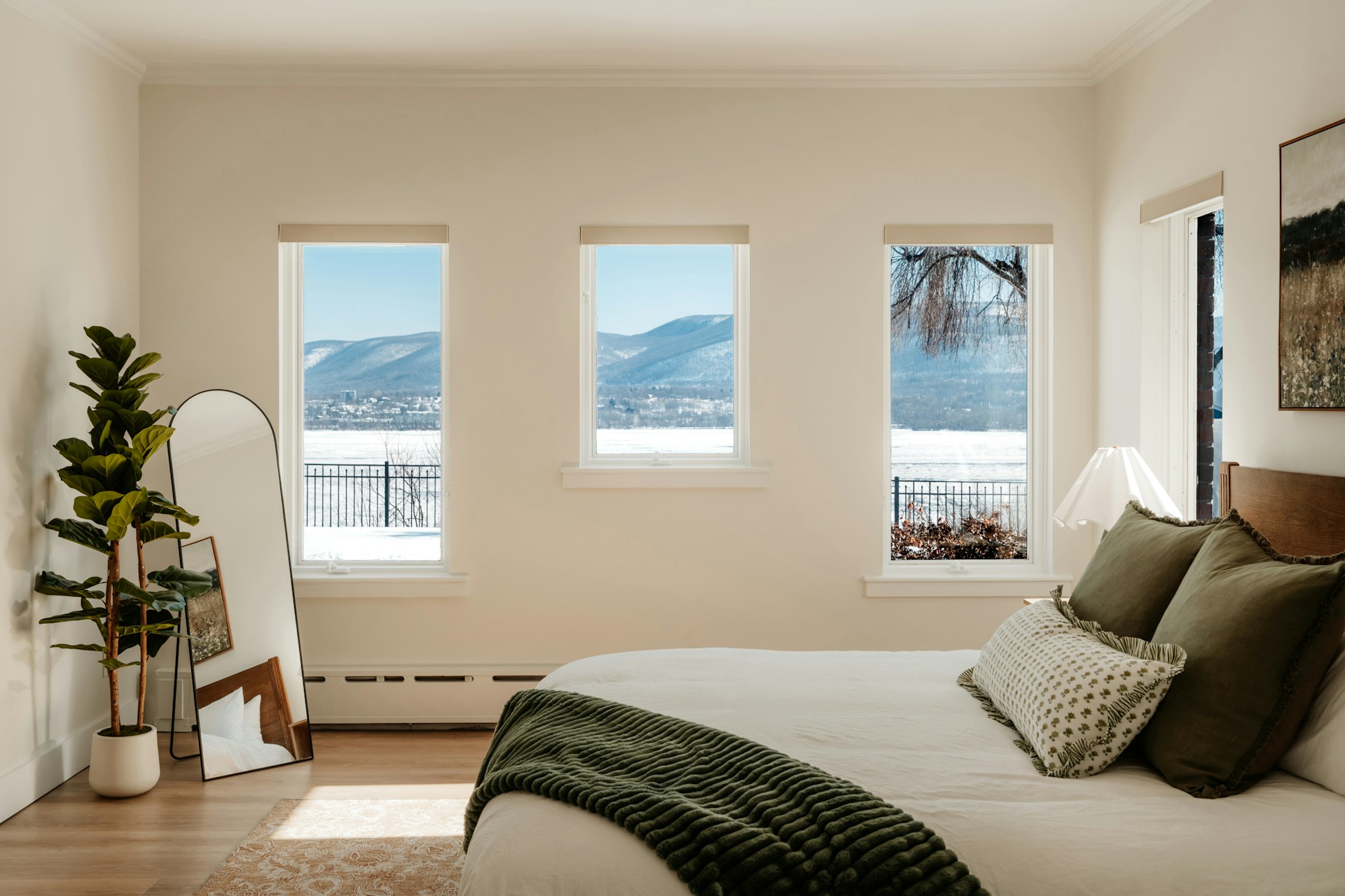 clay-banks-EQc-wkpf4JQ-unsplash Airy holiday bedroom with cream walls, a floor-length mirror, fiddle-leaf fig plant and three windows overlooking a snowy mountain landscape