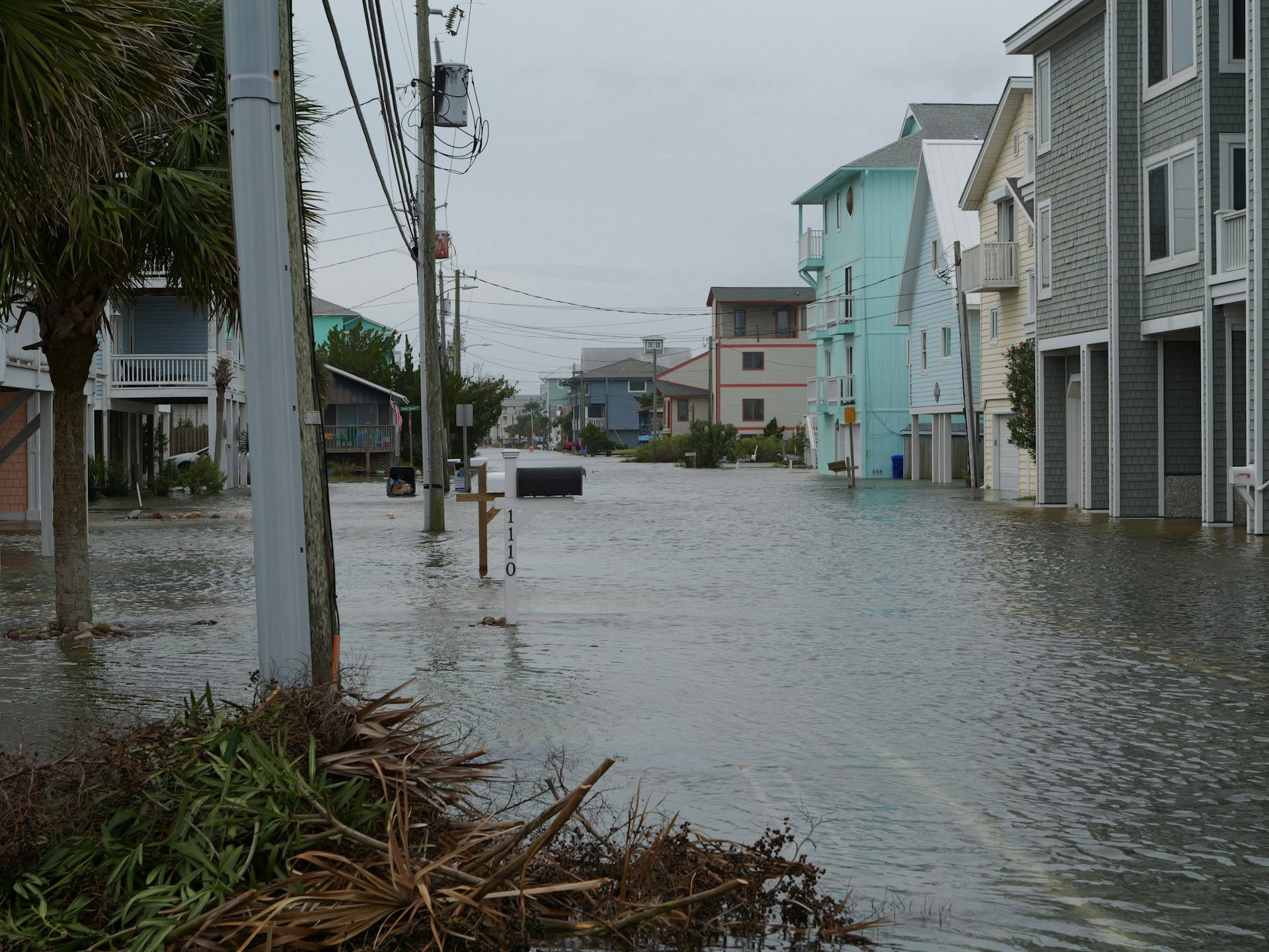 richard-r-EehFb9A3QGs-unsplash Residential street severely flooded after a storm, with water reaching the base of coastal holiday homes and debris washed onto pavements