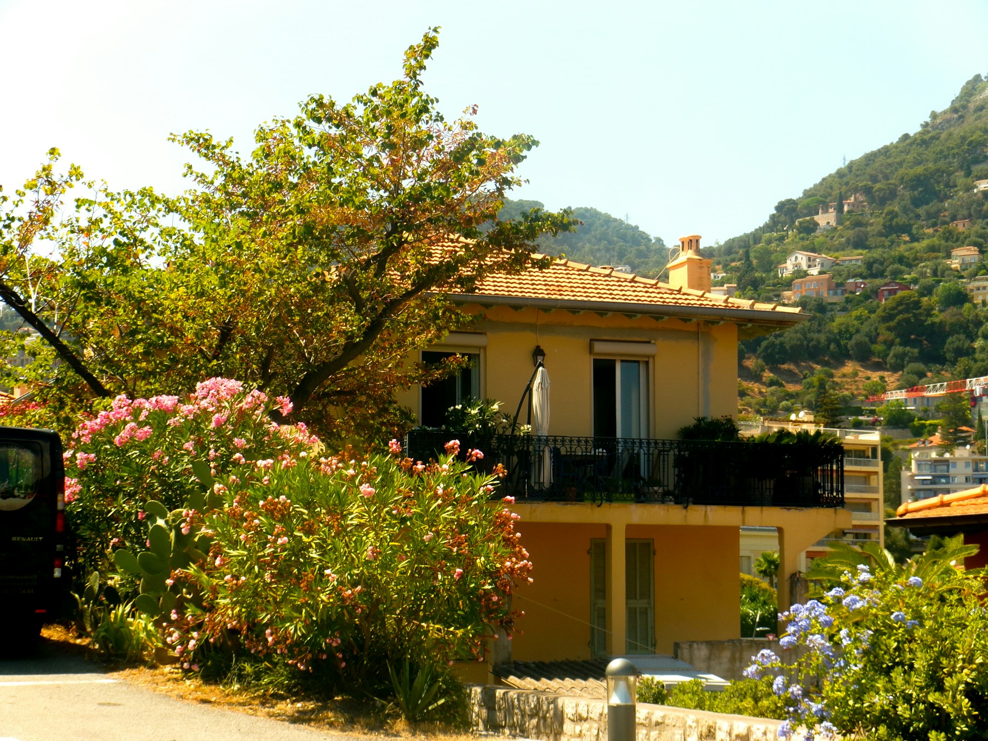 anais-lauret-FpJBjW_PpAc-unsplash Yellow holiday villa with a terracotta roof and iron balcony surrounded by flowering shrubs and wooded hills in the south of France