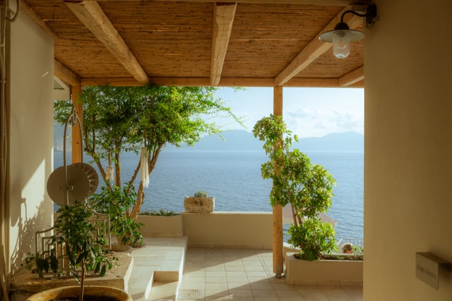christian-harb-UFz38fl-Sjs-unsplash (1) Shaded Mediterranean terrace with a timber pergola, potted plants and a sea view across to an island on the horizon
