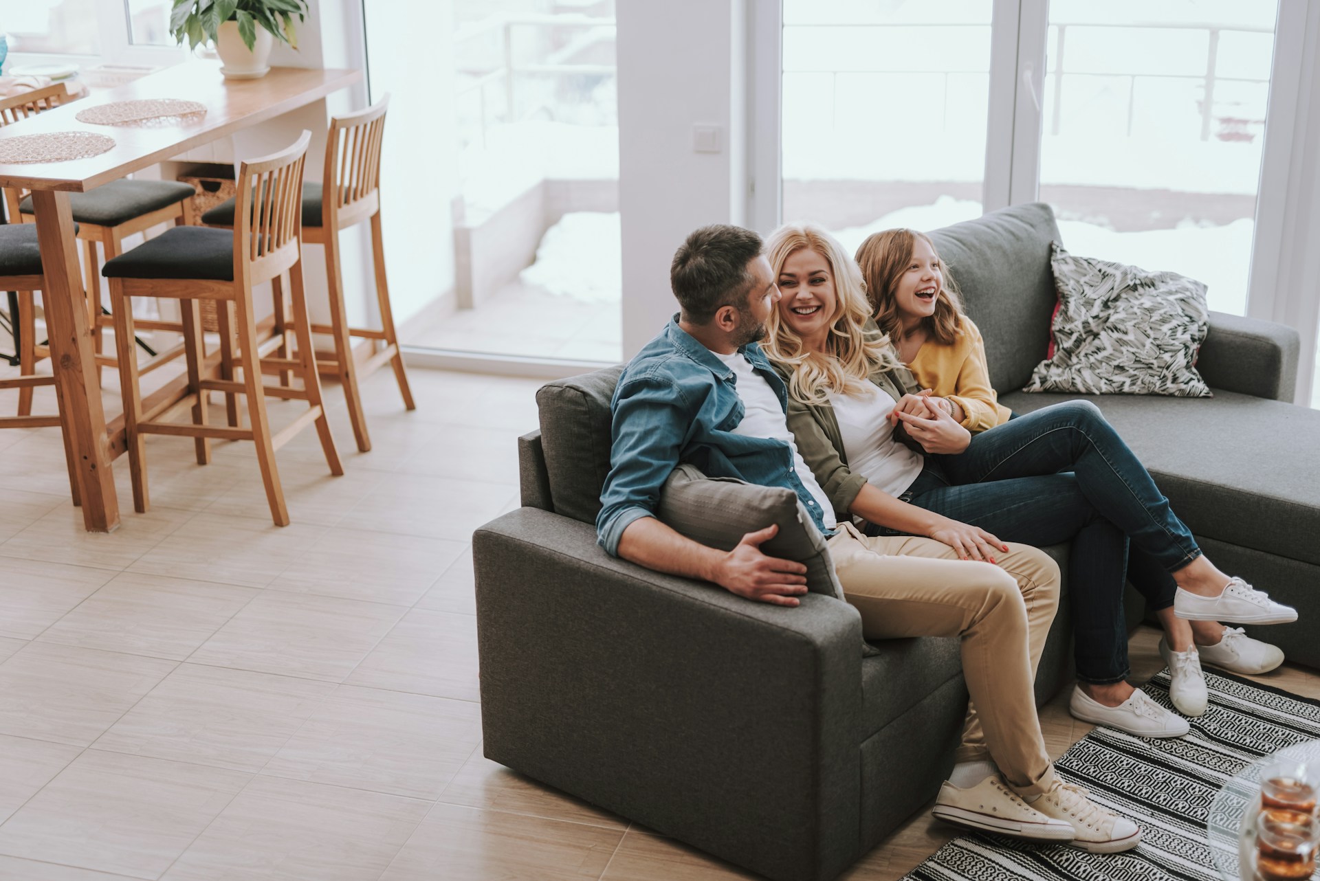 getty-images-EohTOaukYrw-unsplash Smiling family — man, woman and young girl — laughing together on a sofa in a bright open-plan home