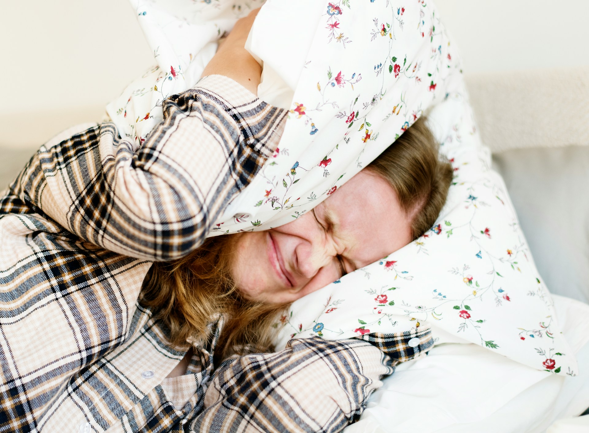 curated-lifestyle via unsplash Frau hält sich ein Kissen über den Kopf um Lärm zu reduzieren
